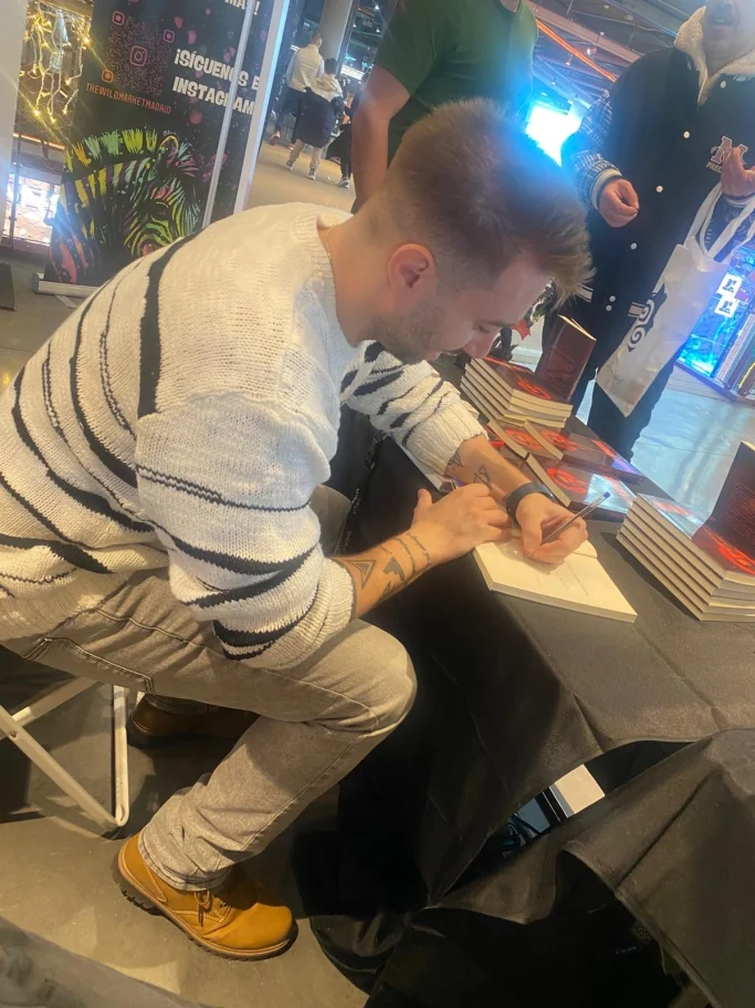 Joven sentado, escribiendo en un cuaderno con un bolígrafo, en un entorno comercial.