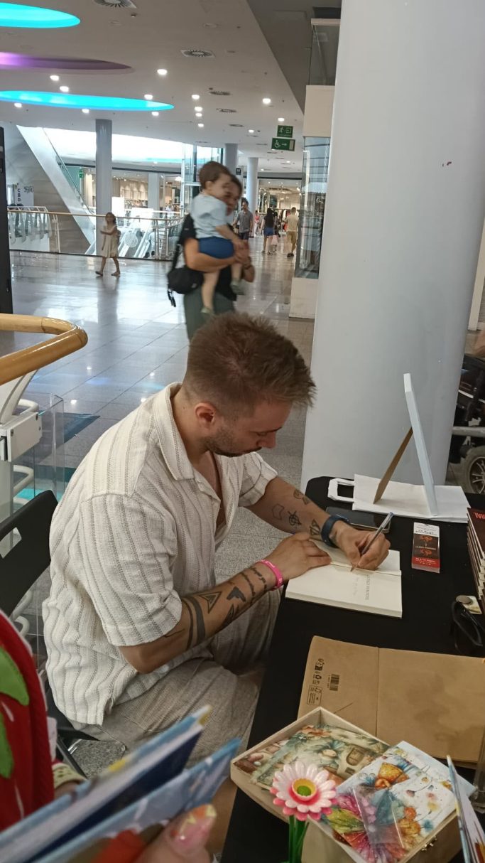 Daniel Moro firmando ejemplares, con otros visitantes en un entorno público.